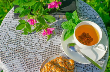 A Cup of green tea with a mint leaf, flowers, and a book on a table in the garden. Evening tea with cookies. Summer village concept. Copy space.