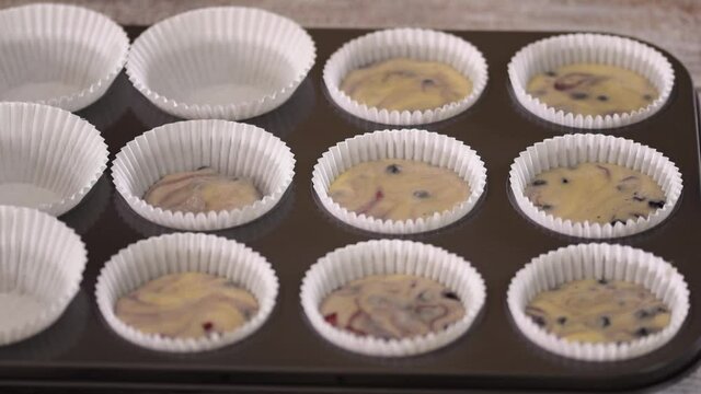 Pouring blueberry batter into muffin cups. Woman baking blueberry muffins.