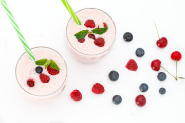Berries smoothies in two glasses with straws on white background. Fresh homemade smoothie with blueberries, raspberries and sour cherries, top view.
