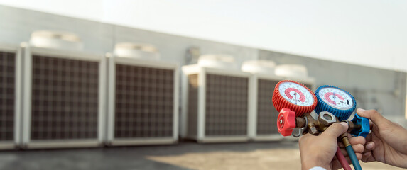 Air repair mechanic using measuring equipment for filling industrial factory air conditioners and...