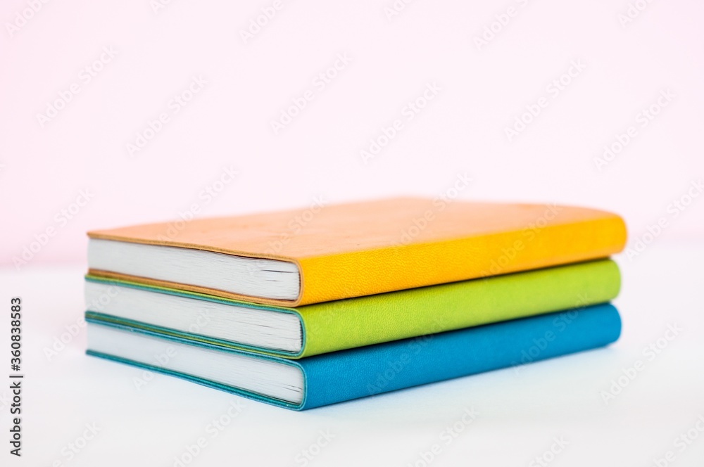 Wall mural Clolseup of orange, green and blue books placed on each other with a white background - Wall murals