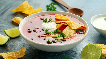 Mexican Chilli bean soup with yogurt, cheese, lime and tortilla chips in white bowl