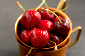 Close up fresh summer fruits, cherries in metal cups, gray background.