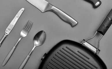 Metal knives with black on a grey table, grill pan, towel. Flat lay, layout with copy space.
