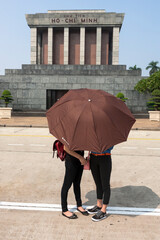 Two young students hide behind an umbrella in front of Ho Chi Minh's Mausoleum, Hanoi, Vietnam