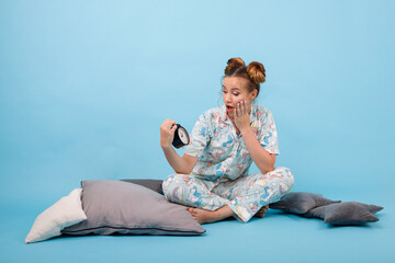 Fototapeta na wymiar girl in pajamas and with an alarm clock on a blue background. Good morning