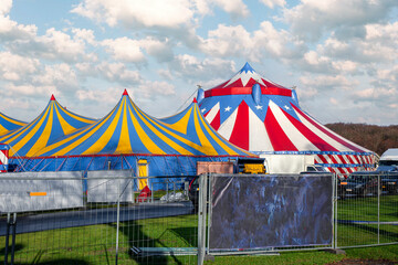 Red and white circus tent topped with bleu starred cover against a sunny blue sky with clouds © Ankor light