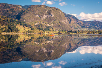 Two people row on Lake Bohinj in Slovenia on a clear autumn day. Reflection of the Alps in water. Water activity