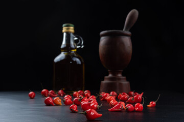 Peppers, olive oil and wooden mortar on black background, selective focus