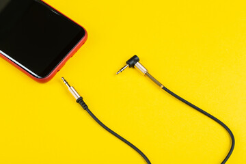 Obraz premium Close-up Jack plug and a cable with phone on a yellow background.