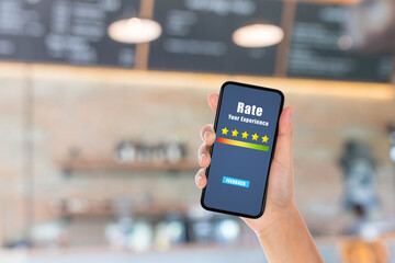 Customer Feedback and Satisfaction Concept : Hand holding smartphone to give best service ranking with blurry image of cafe restaurant or coffee shop in background.