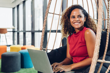 Attractive happy creative african american woman using computer and smiling while sitting in modern...