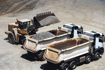 Dumper trucks being loaded on ore mine, works at open pit mine. Wheel loader loading dumper trucks © aboutmomentsimages