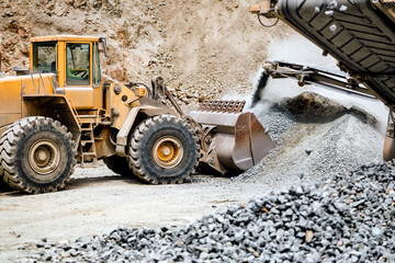 Heavy duty wheel loader machine loading rocks in the open mine, iron ore mining details. Industrial machinery working with rock breaker and crusher, dumper trucks