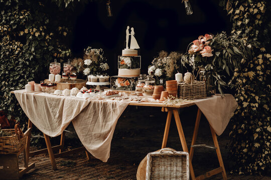 Candy bar. White wedding cake decorated by flowers standing of festive table with deserts, strawberry tartlet and cupcakes. Wedding. Reception Tartlets