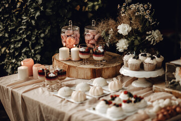Candy bar. White wedding cake decorated by flowers standing of festive table with deserts,...