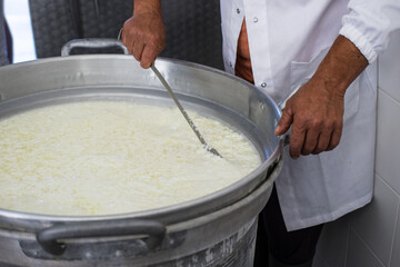 Man stirs with a large metal trowel through a hot big zinc cauldron with curled milk. The curdled...