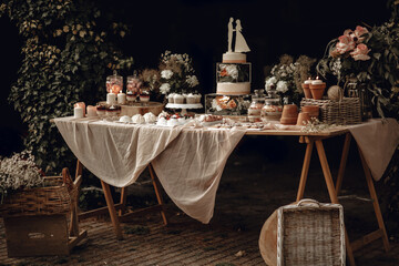 Candy bar. White wedding cake decorated by flowers standing of festive table with deserts,...