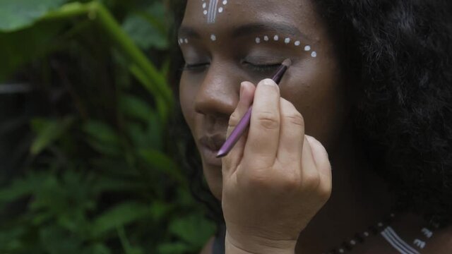 African girl with makeup and painted ethnic lines on the body sitting in a tropical garden