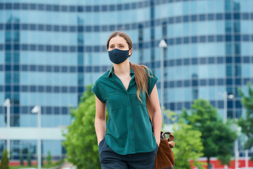 A young woman in a medical face mask to avoid the spread of coronavirus walking in the center of the city. A girl with long hair keeping social distance wears a protective face mask in downtown.