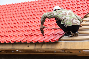 Workers install red metal tiles on the roof