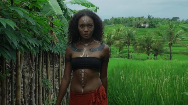 Africa girl with makeup and painted etnic lines on the body walking in a tropical garden