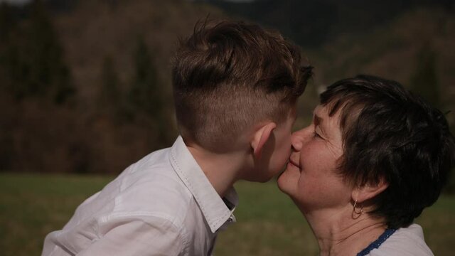 Grandson kisses grandmother on the cheek. Relationships between generations, family. Outside, a bright sunny day