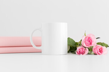 Mug mockup with books and a bouquet of pink roses on a white table.