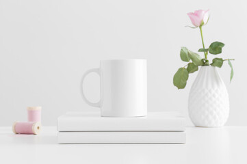 Mug mockup with a pink rose and books on a white table.