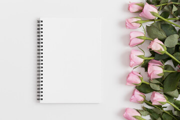 Top view of a notebook mockup with pink roses on a white table.