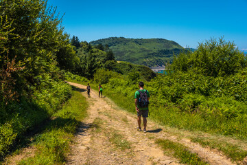 Fototapeta premium Three friends along the path reaching the coastal town of Orio, Guipuzcoa, Basque Country. Excursion from San Sebastián to the town of Orio through Mount Igeldo walking 3 friends.