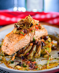 A seafood dinner serve of a piece of Salmon on top of grilled vegetables, in a round white plate
