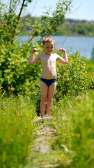 Portrait of a funny little boy standing barefoot on path near pond