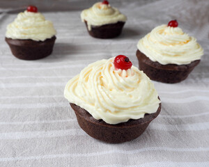 four gluten-free cupcakes with cream cheese and redcurrant berries on a light side table . homemade cake