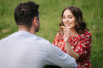 Happy couple spend time outdoors on mini picnic. Attractive woman and handsome man sits on red blanker by the big tree
