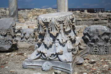 Part of a column with an ornament on the background of old destroyed buildings, from which only stones remained