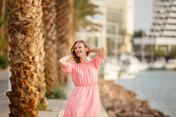 Young woman on a beach near palm trees weared in pink dress. Tropic vacation. Sea relax and rest. Spending a time on beach. Enjoying Happy time. Smiling female in lagoon. Summer holiday local tourism