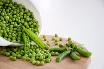 Fresh green peas and pods in white bowl on wooden cutting board. Healthy nutrition, farm harvest