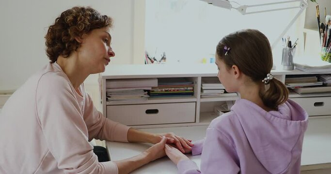 Back view compassionate mother holding hands of upset crying adolescent daughter, supporting telling advices against school bullying. Affectionate worrying mom giving psychological help to teen girl.