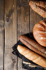 Variety of loaves of bread and baguette on wooden table background
