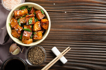 Flat lay view at stir fried tofu cubes with chives in clay dish on wooden kitchen table with napkin chives pepper garlic and soy sauce aside - obrazy, fototapety, plakaty