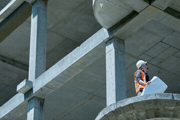 An architect in a protective suit at a height compares the plan of completed works with the drawing in his hands