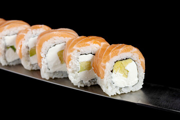 Japanese rolls and seafood sushi on a katana sword on a black background