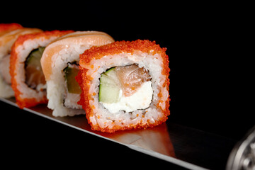 Japanese rolls and seafood sushi on a katana sword on a black background