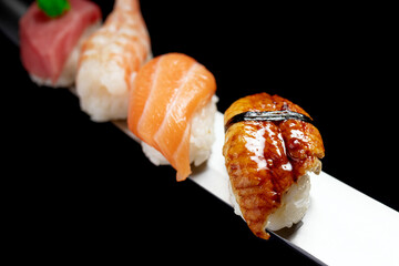 Japanese rolls and seafood sushi on a katana sword on a black background