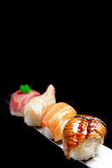 Japanese rolls and seafood sushi on a katana sword on a black background