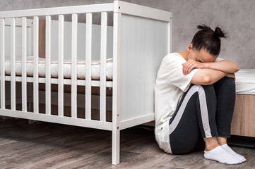 young woman sits sad by the crib. Postpartum Depression Concept