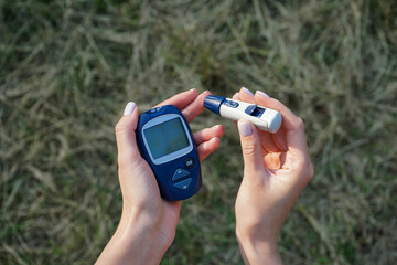 A young woman holds in her hands a glucometer and a lancet pen on the street. Diabetes control. Woman checks blood sugar level for diabetes.
