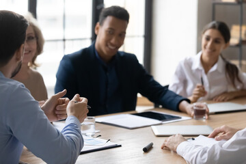 Interested diverse employees listening to mentor coach at meeting close up, sitting at table in boardroom, team leader speaking, leading briefing, training interns, explaining project strategy