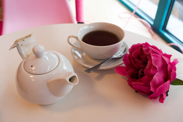 Fototapeta na wymiar ceramic white teapot and Cup of tea on the table in the cafe and decor in the form of a pink rose flower